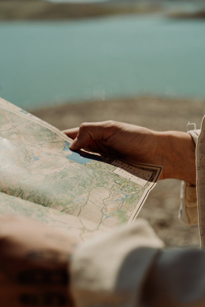 Hands holding a map outdoors with a scenic lake and landscape view in the background.